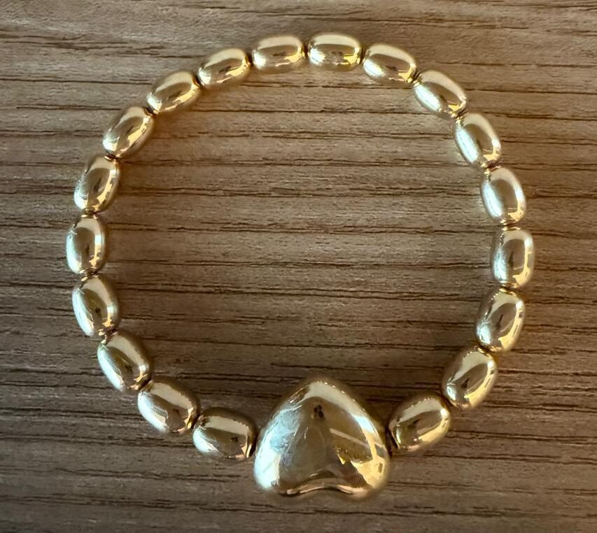Pulseira com elástico, toda de contas gordinhas banhadas a ouro com um coração no centro. Foto com duas figurativo. Valor unitário.