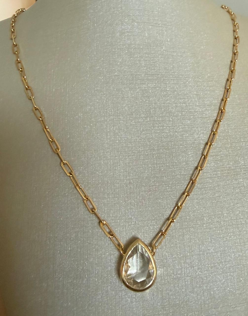 Colar curto, com correntes em elos finos, com um pingente lapidado formato gota de cristal transparente.