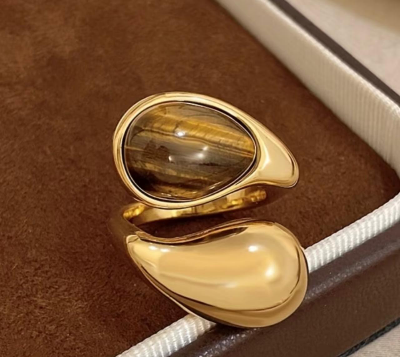 Anel regulável aberto em cima, com uma gota em pedra Olho de Tigre e do lado uma gota no banho de ouro.