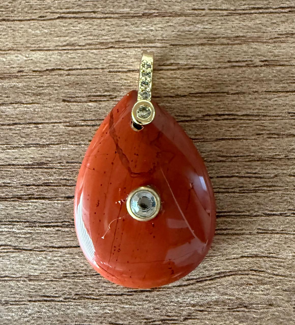 Pingente em pedra natural no formato gota no tom terroso, alça cravejada de mini Zircônias com uma Zircônia incrustada no meio da gota. Colar apenas sugestivo.